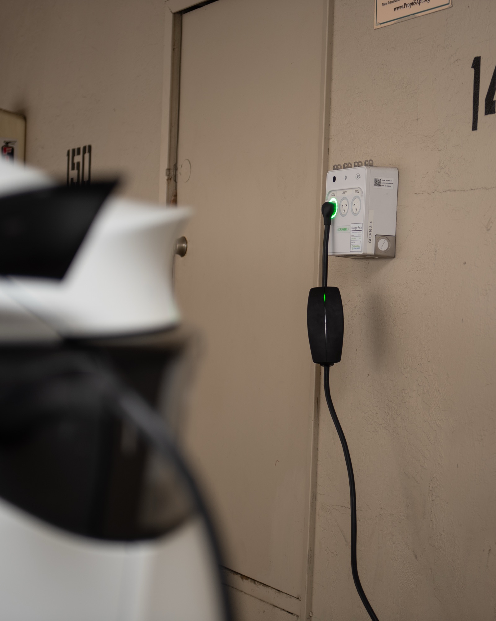 A mobile charge cord plugged into the Level 1 outlet of a wall-mounted PowerPort3, indicator lit green